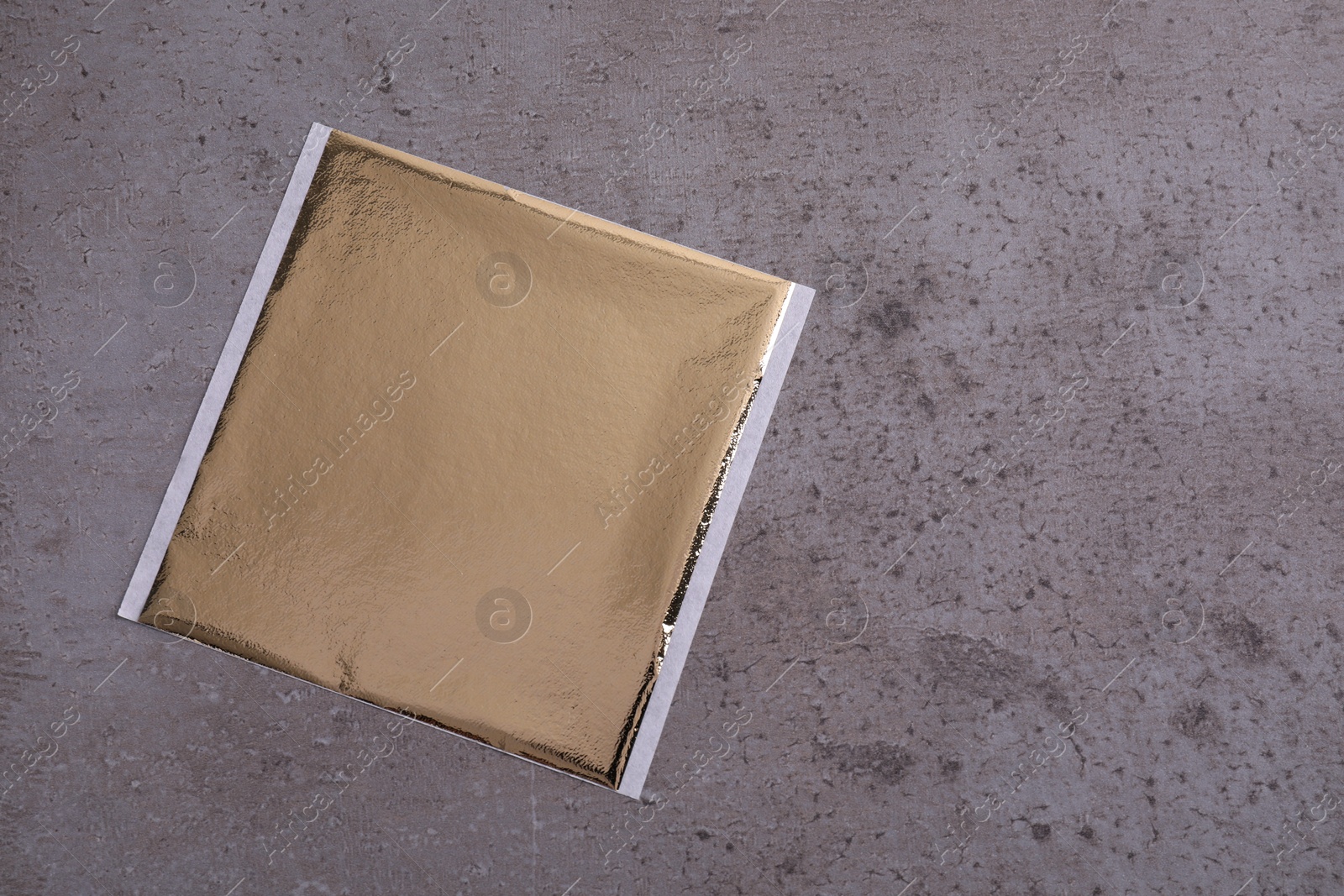 Photo of Edible gold leaf sheet on grey textured table, top view. Space for text