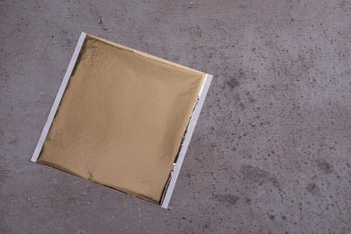Edible gold leaf sheet on grey textured table, top view. Space for text