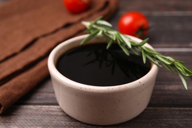 Photo of Bowl with balsamic vinegar, rosemary and tomatoes on wooden table, closeup