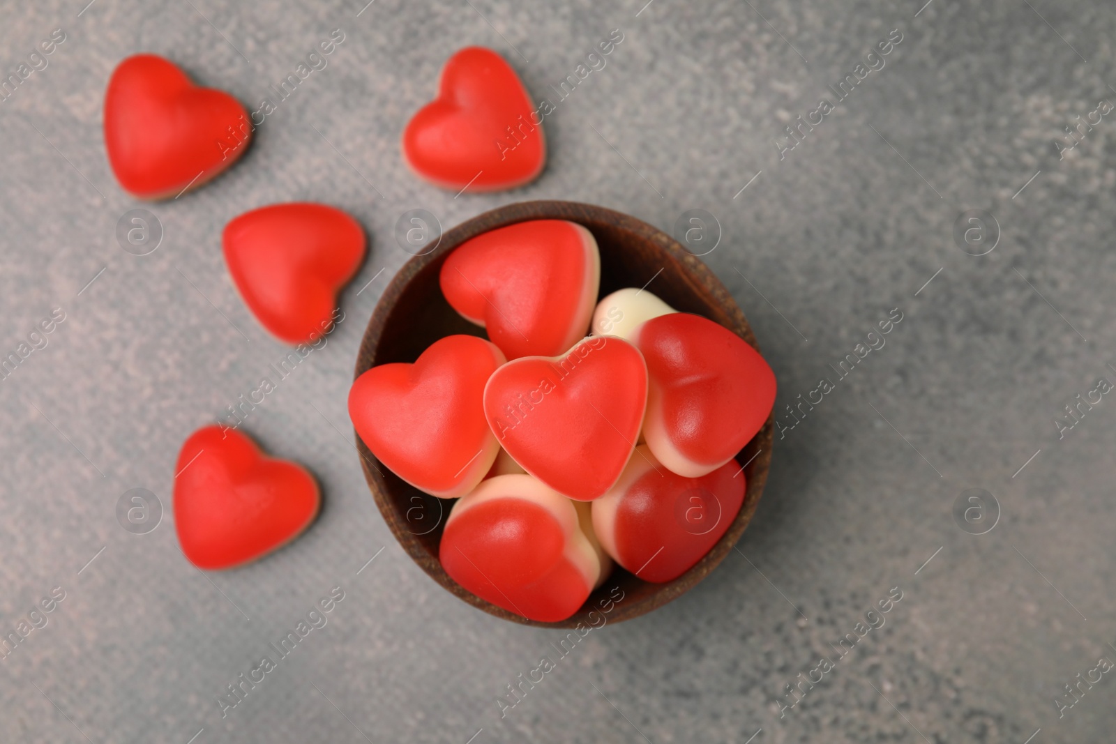 Photo of Bowl and delicious heart shaped jelly candies on grey table, flat lay