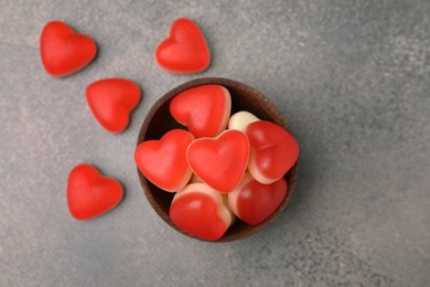 Bowl and delicious heart shaped jelly candies on grey table, flat lay