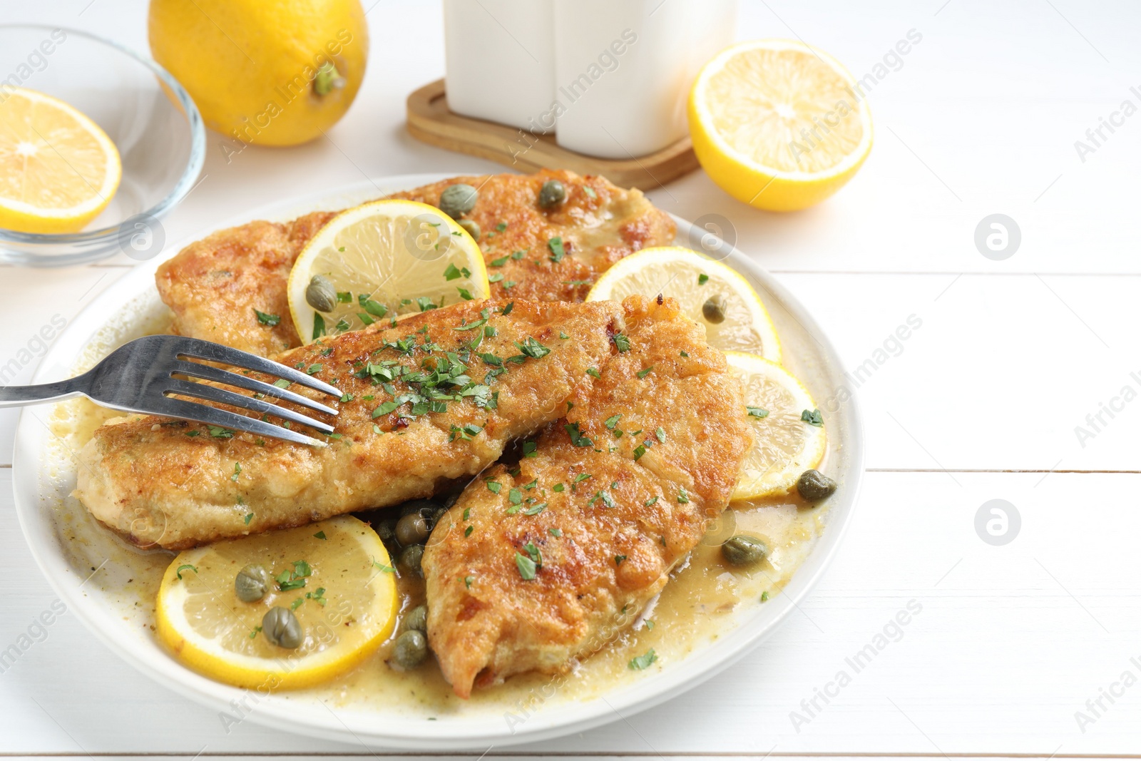 Photo of Delicious chicken piccata served on white wooden table, closeup