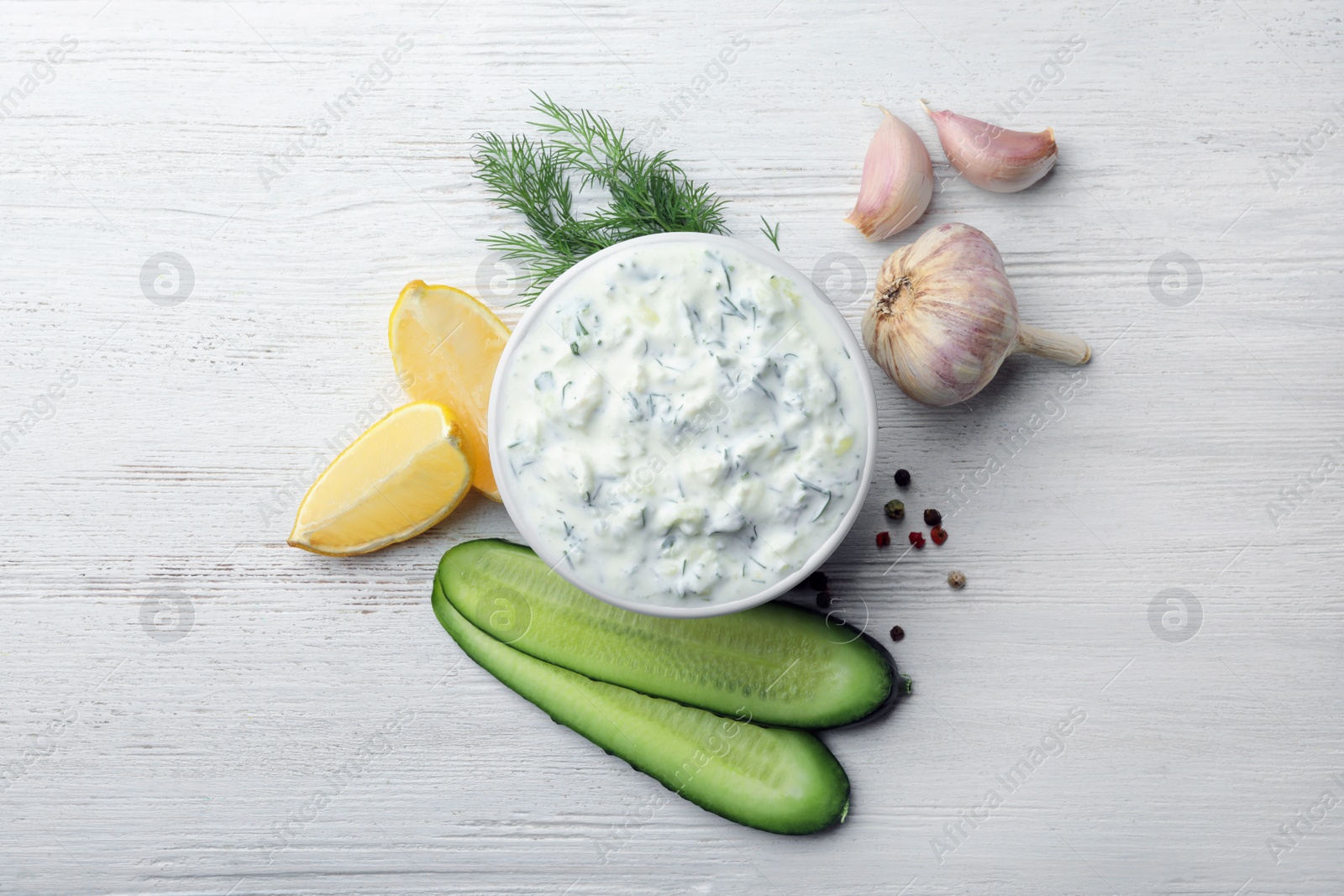 Photo of Tzatziki cucumber sauce with ingredients on wooden background, flat lay