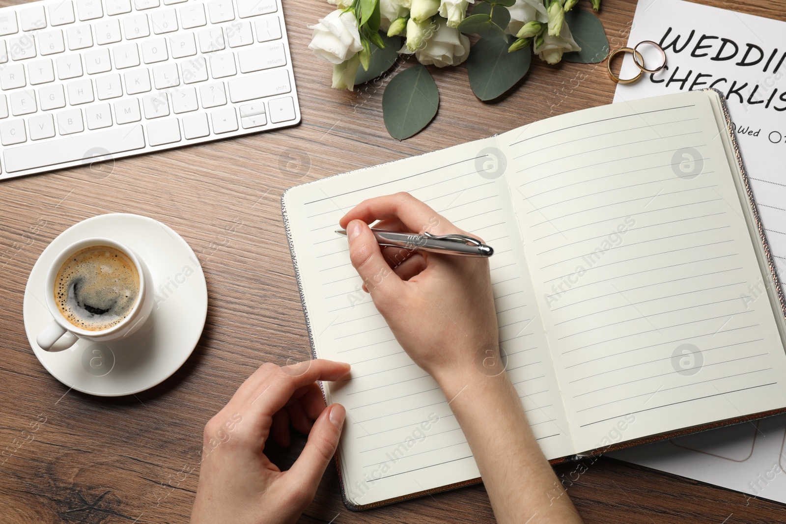 Photo of Woman writing in Wedding Planner at wooden table, top view