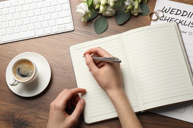 Photo of Woman writing in Wedding Planner at wooden table, top view