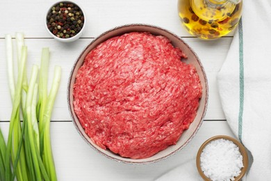 Bowl of raw fresh minced meat and ingredients on white wooden table, flat lay