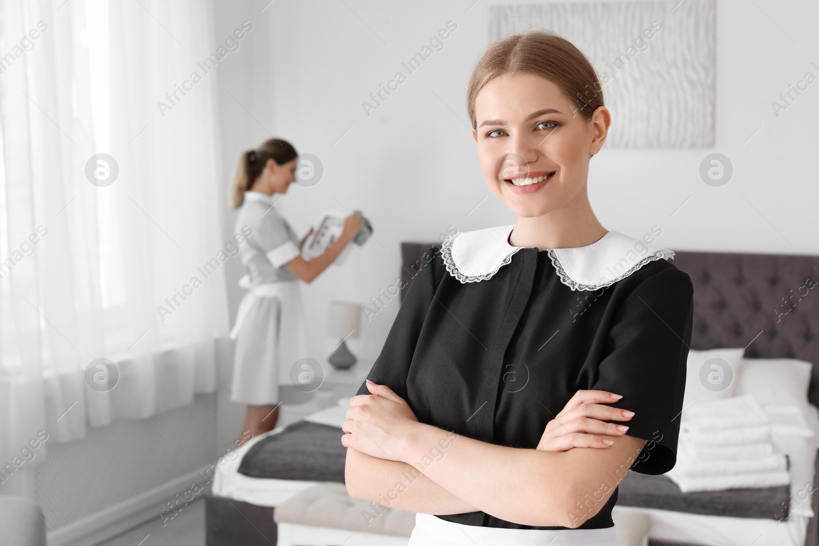 Photo of Young chambermaid in uniform standing near bed indoors