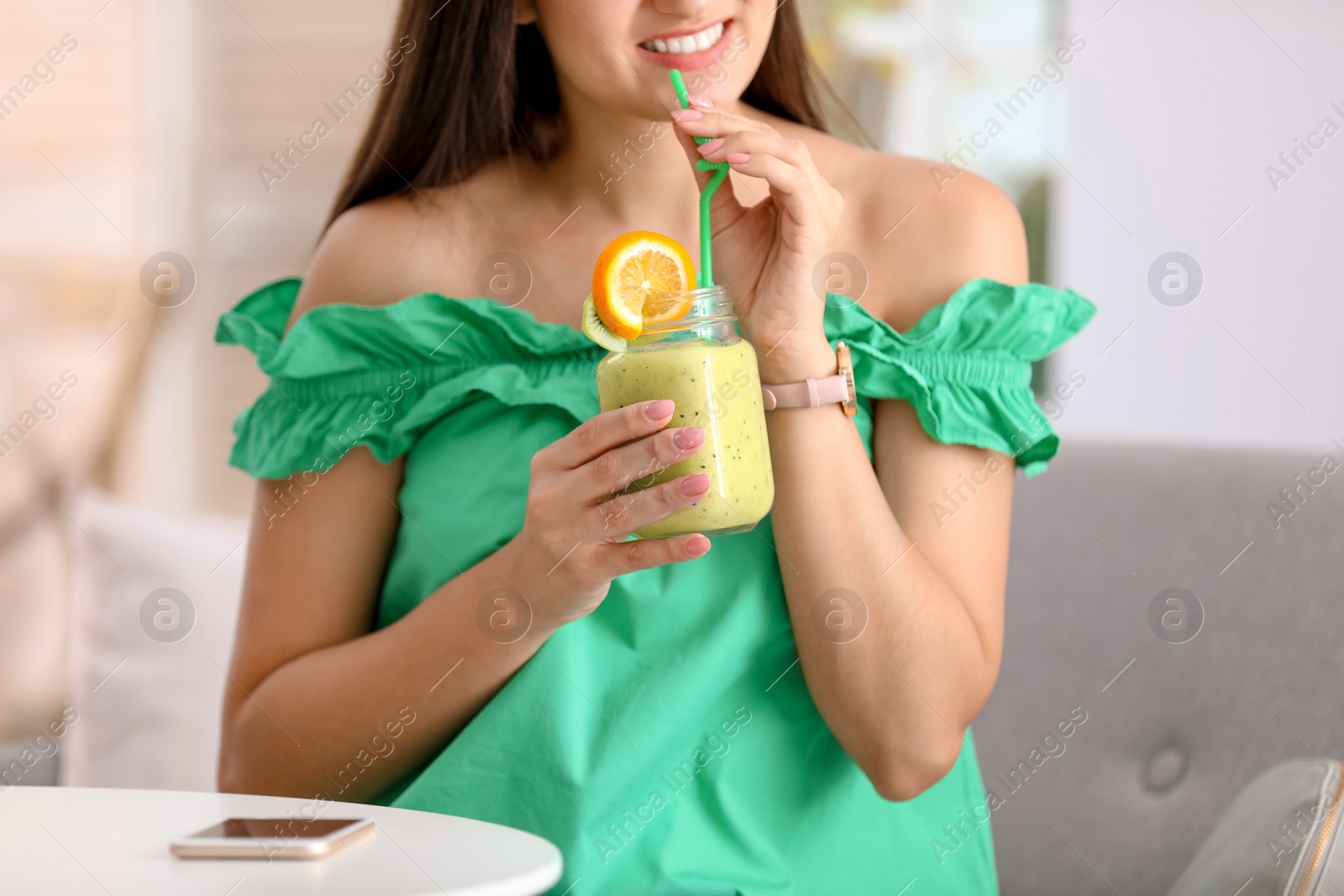 Photo of Young woman with tasty healthy smoothie at table, indoors