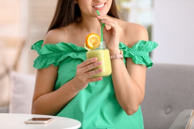 Young woman with tasty healthy smoothie at table, indoors