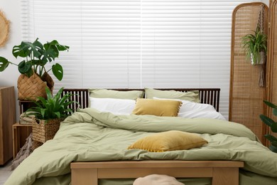 Comfortable bed and beautiful green houseplants in bedroom