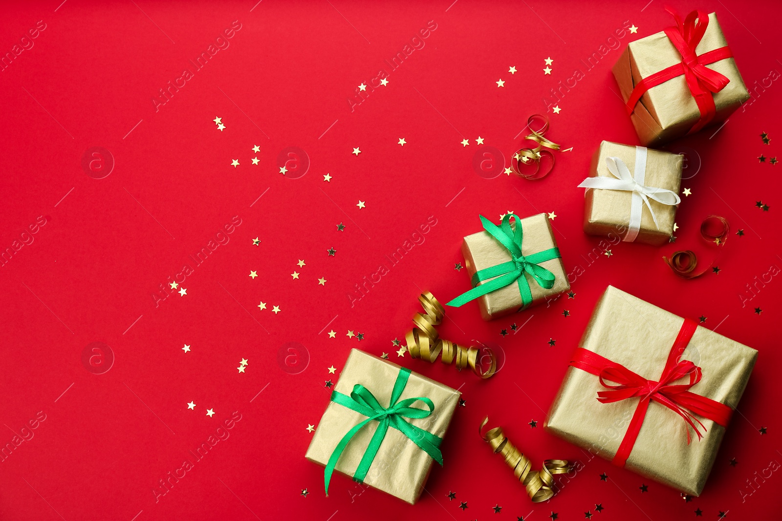 Photo of Christmas gift boxes and shiny confetti on red background, flat lay. Space for text