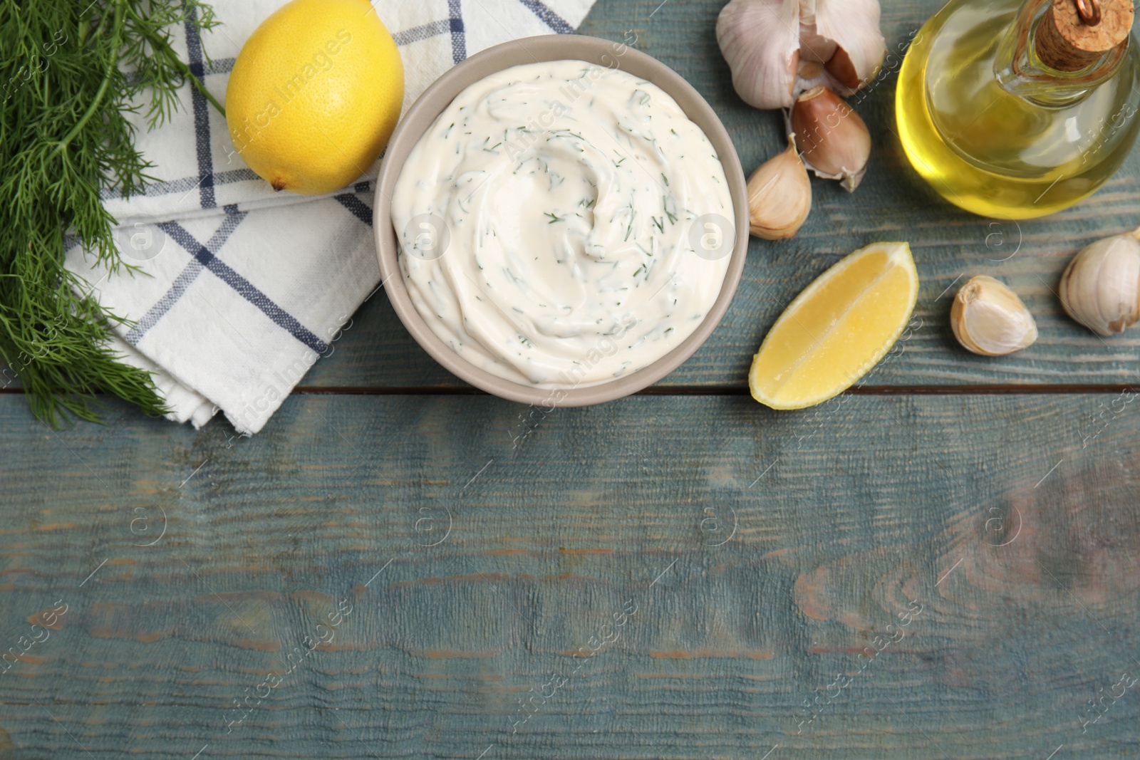 Photo of Tasty creamy dill sauce and ingredients on blue wooden table, flat lay. Space for text