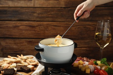 Photo of Woman dipping piece of bread into fondue pot with melted cheese at table with snacks, closeup