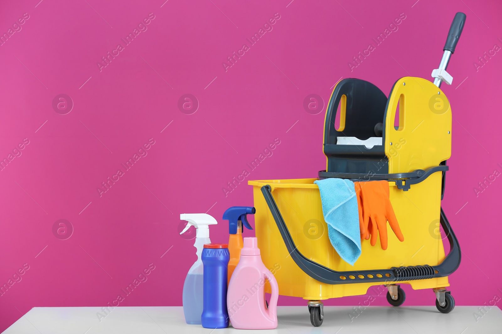 Photo of Mop bucket with cleaning supplies on color background