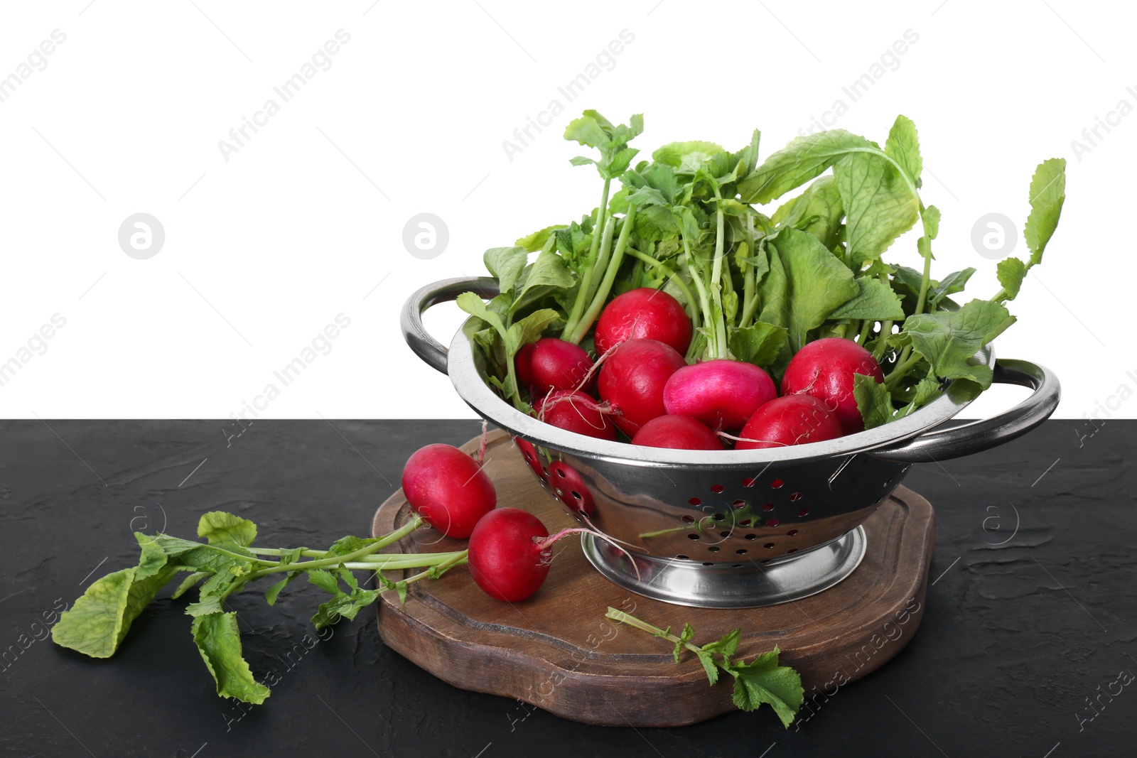 Photo of Metal colander with fresh radishes on black textured table against white background