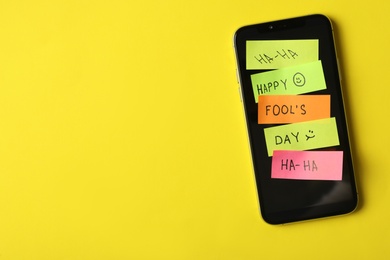 Smartphone covered with stickers and space for text on yellow background, top view. April fool's day