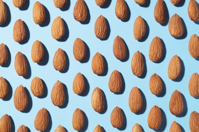 Photo of Delicious raw almonds on light blue background, flat lay