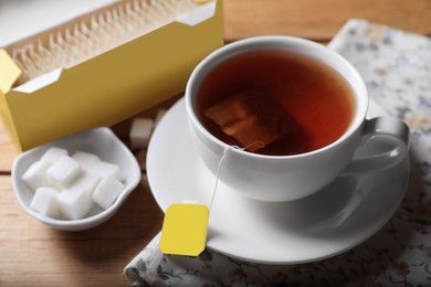 Photo of Tea bags package, sugar and cup of hot drink on wooden table, closeup