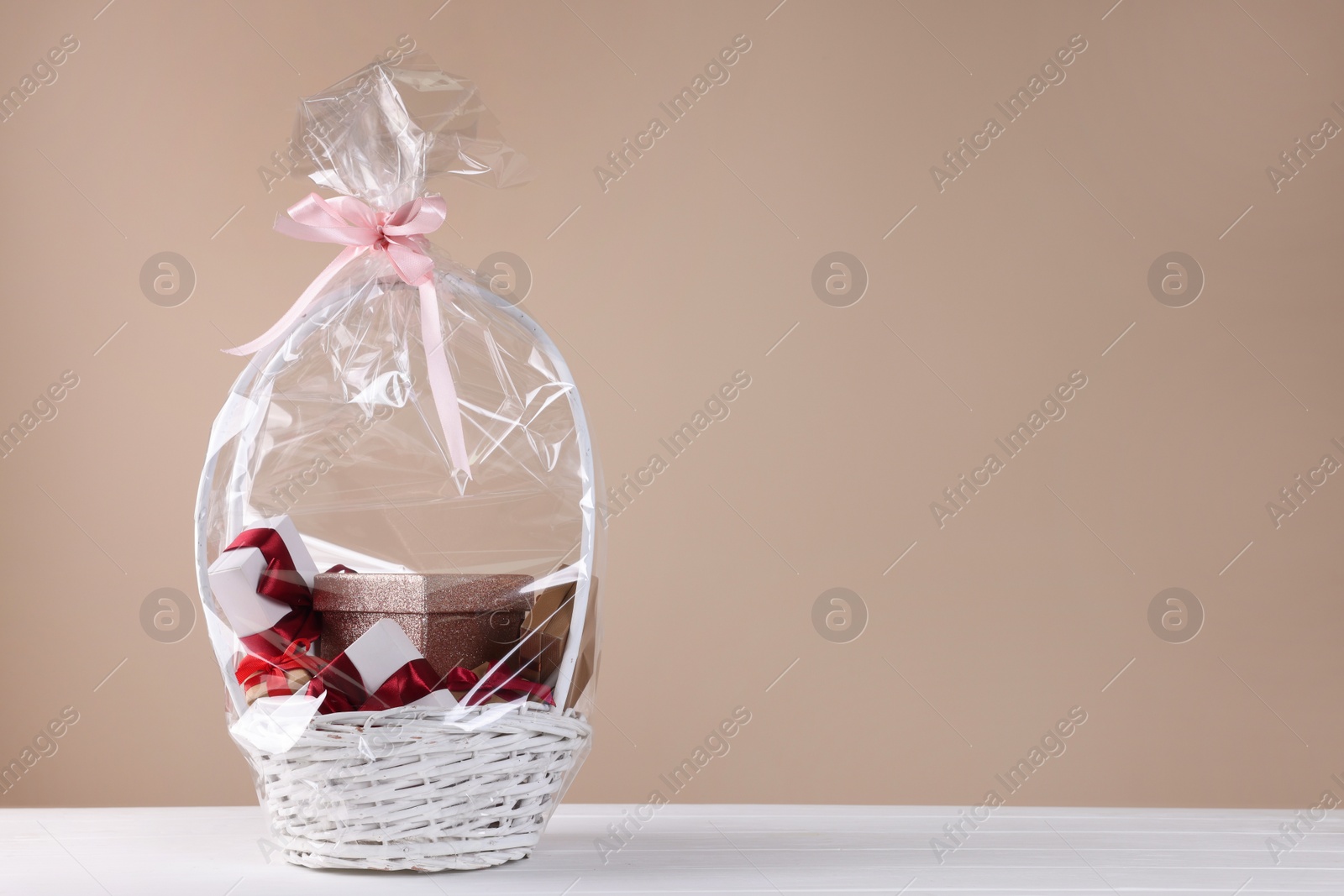 Photo of Wicker basket full of gift boxes on white table against beige background. Space for text