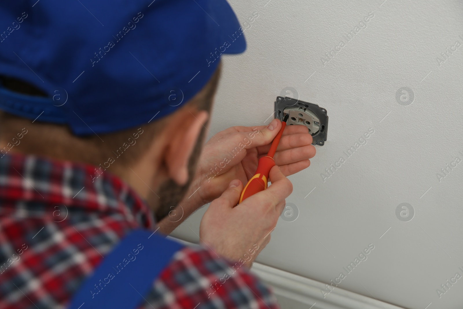 Photo of Electrician with screwdriver repairing power socket indoors, closeup