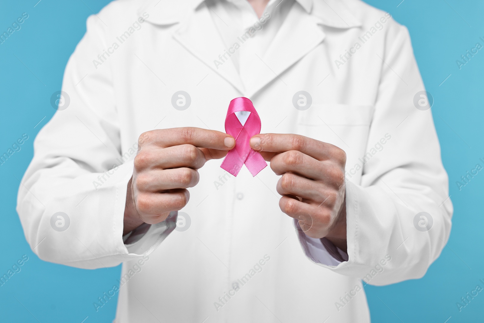 Photo of Mammologist giving pink ribbon on light blue background, closeup. Breast cancer awareness