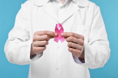 Photo of Mammologist giving pink ribbon on light blue background, closeup. Breast cancer awareness