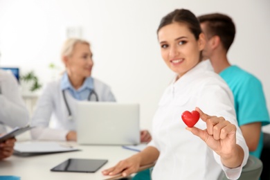 Photo of Female doctor holding small heart at table in clinic. Cardiology conference