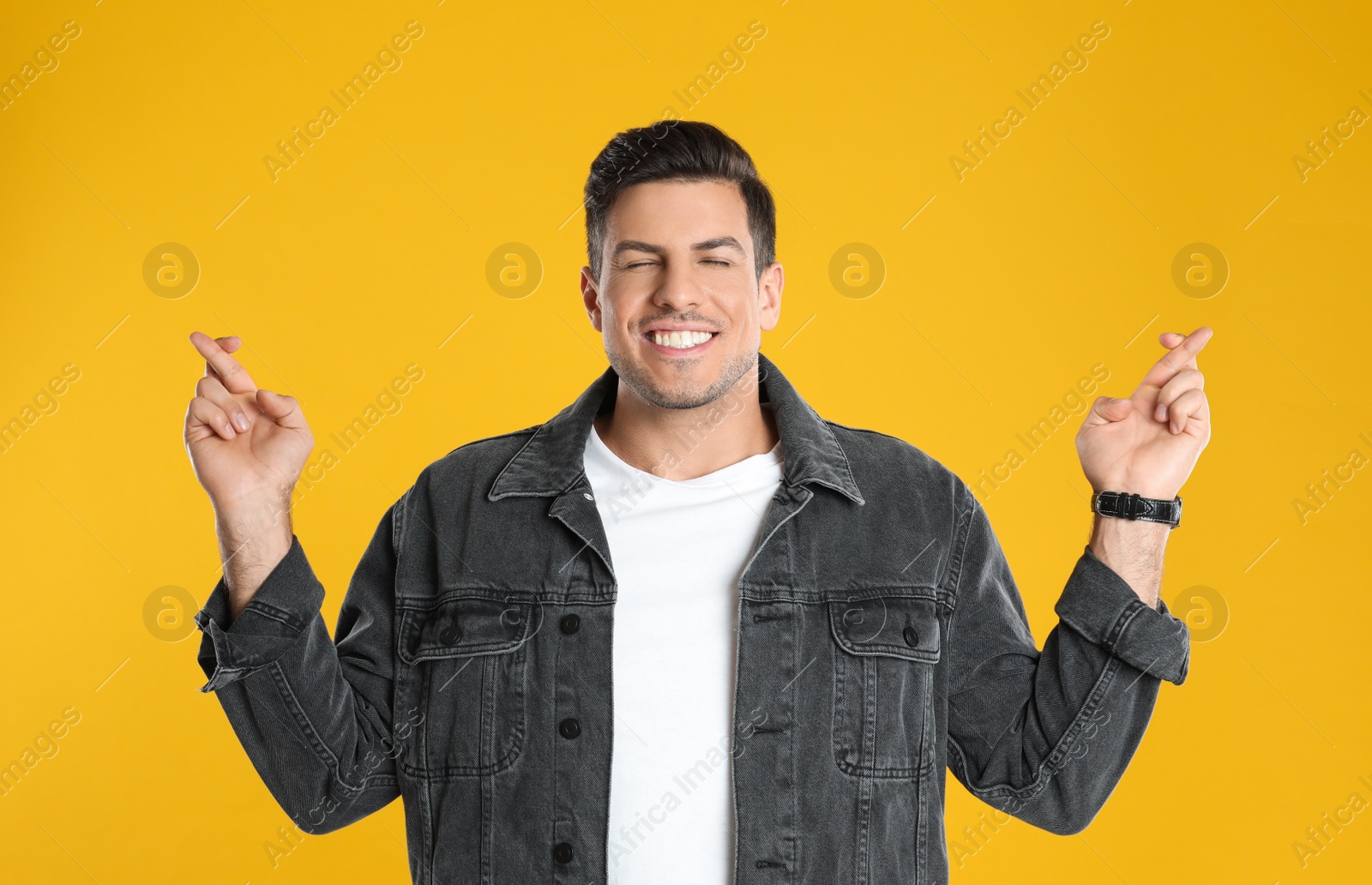 Photo of Man with crossed fingers on yellow background. Superstition concept