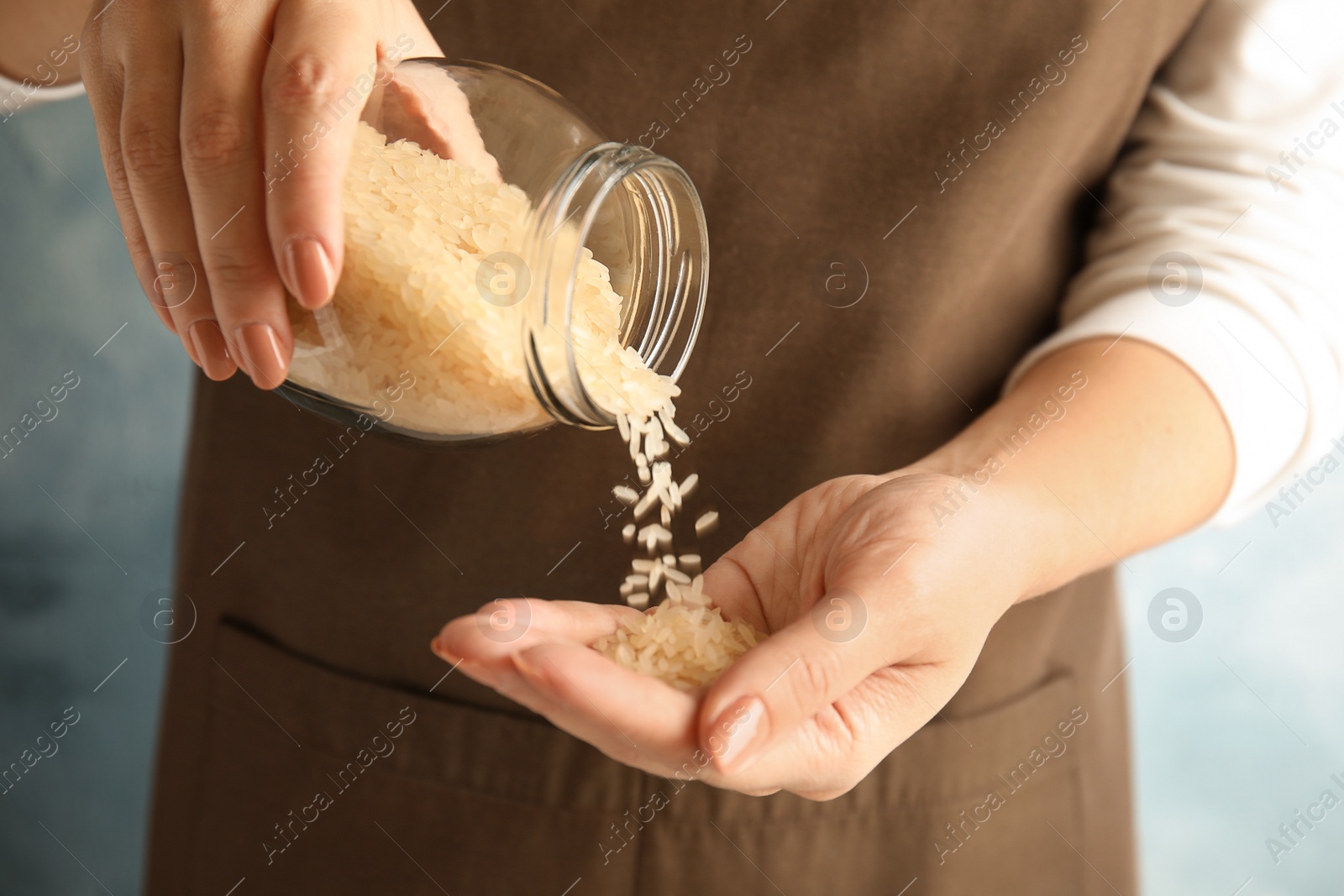 Photo of Woman pouring uncooked rice from jar into hand on color background, closeup