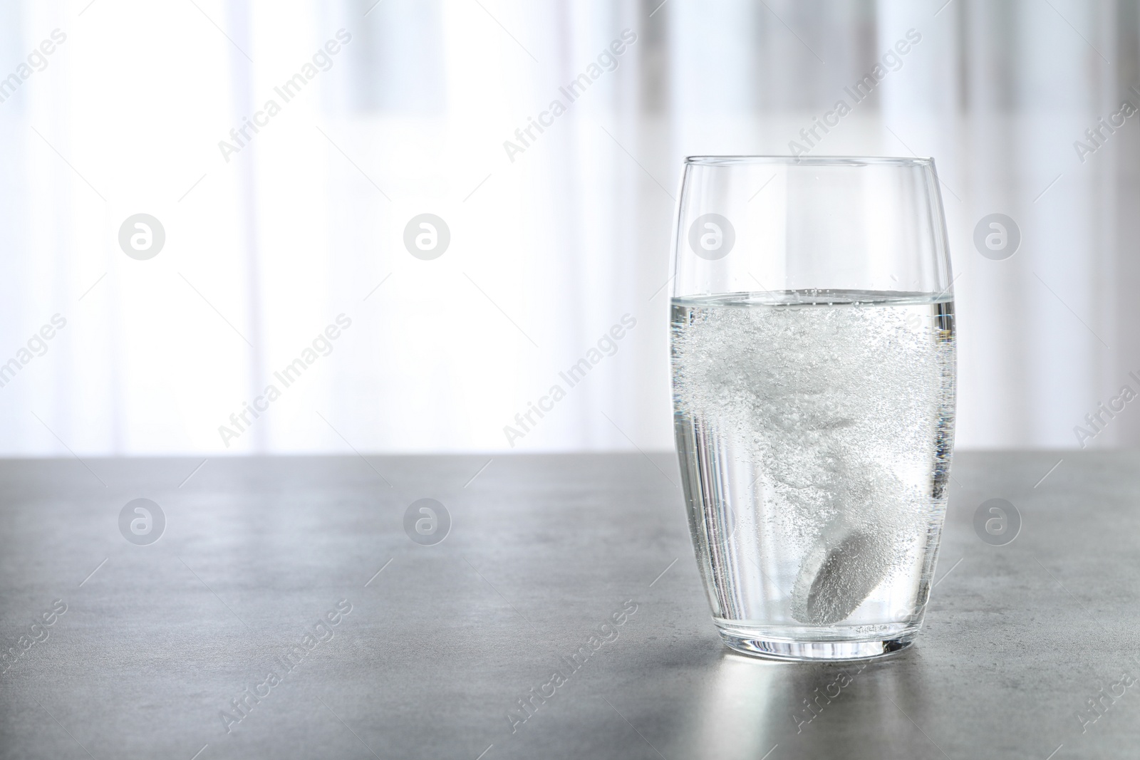 Photo of Glass with effervescent tablet on grey table indoors, space for text. Medical care