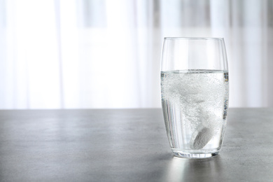 Photo of Glass with effervescent tablet on grey table indoors, space for text. Medical care