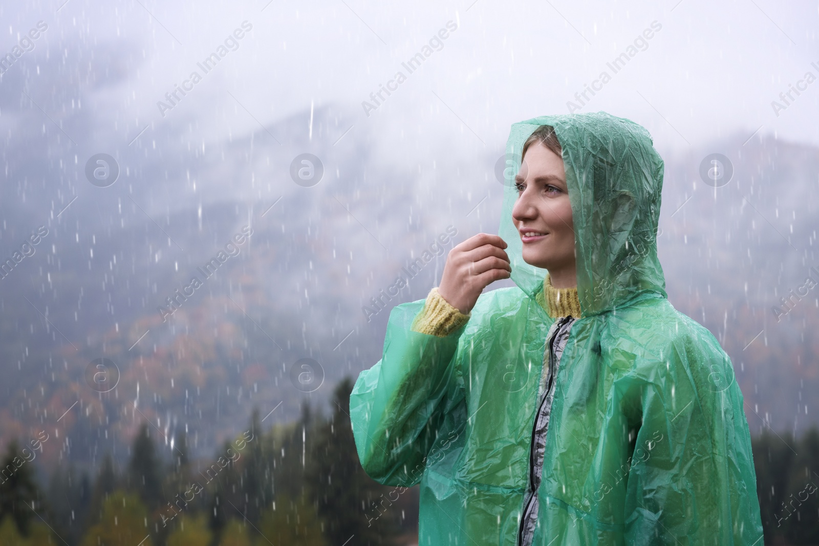 Photo of Young woman in raincoat enjoying mountain landscape under rain