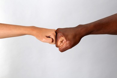 Woman and African American man making fist bump on light grey background, closeup