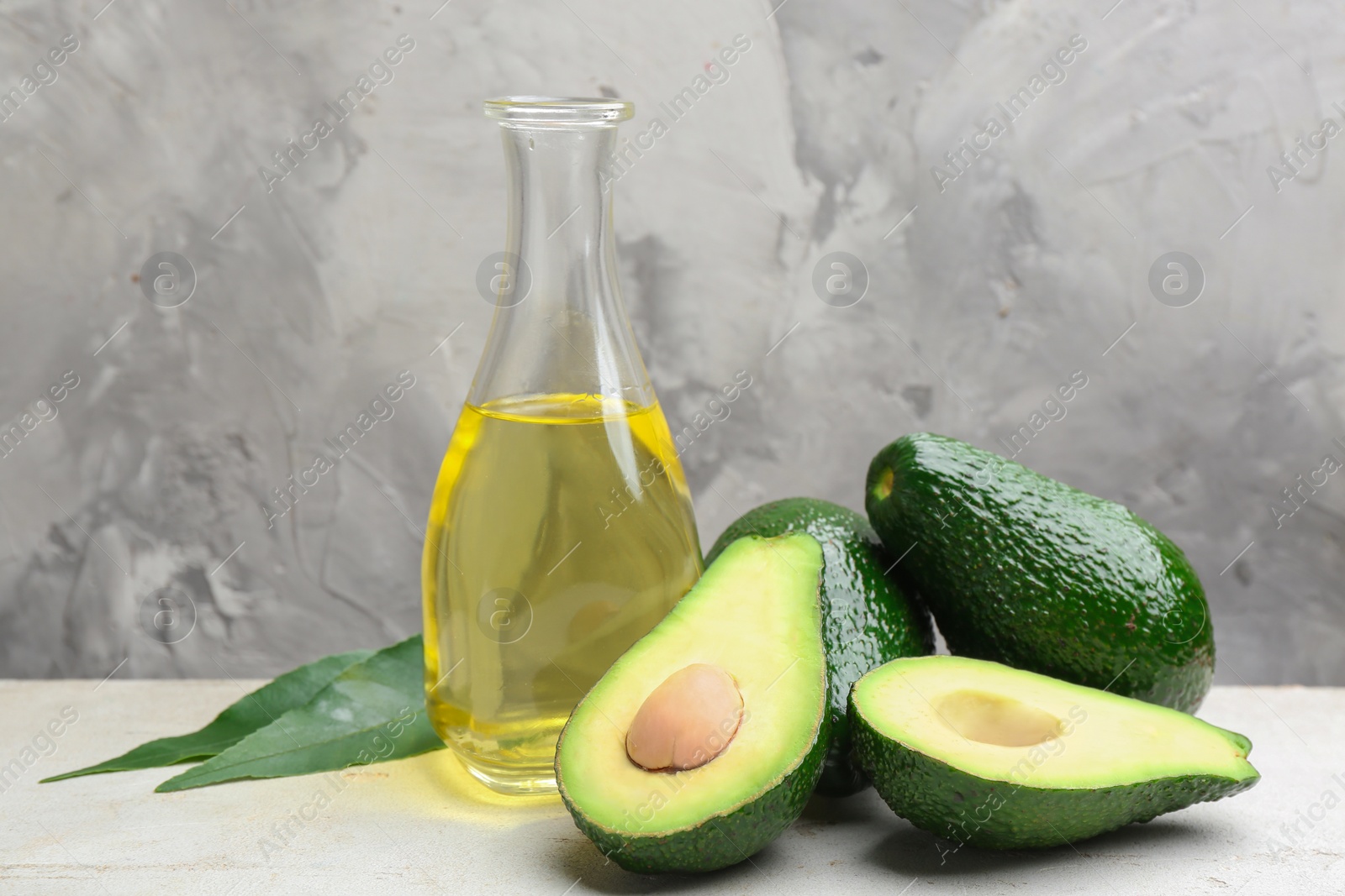 Photo of Bottle of natural oil and avocados on table against grey stone background