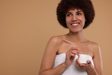 Photo of Beautiful young woman holding body cream on beige background, space for text