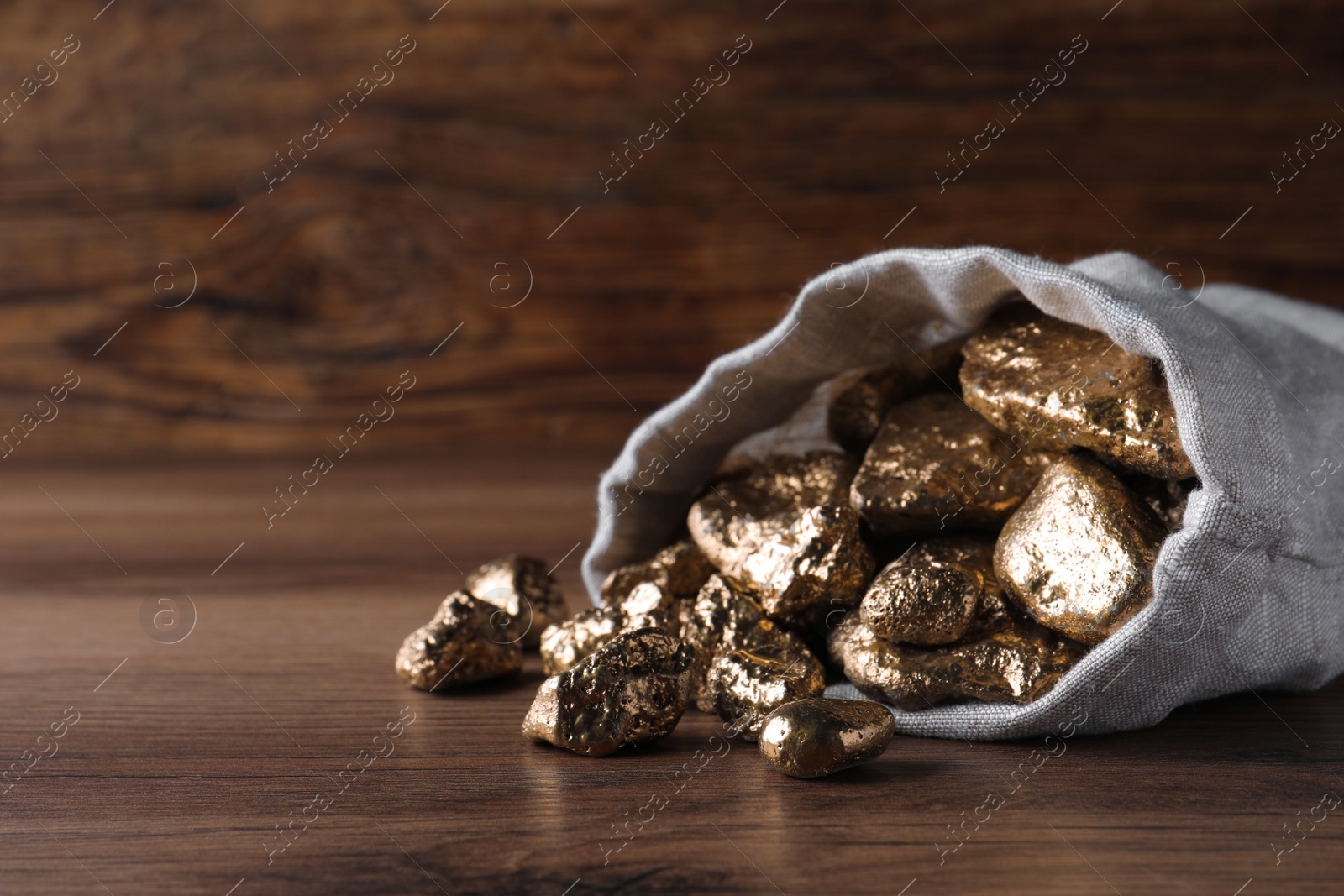 Photo of Overturned sack of gold nuggets on wooden table, closeup. Space for text