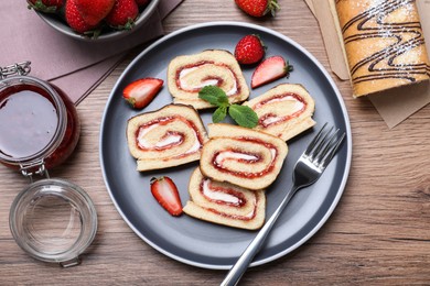 Tasty cake roll with strawberry jam and cream on wooden table, flat lay