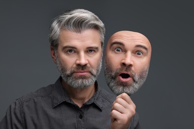 Image of Man holding mask with his facial expression on grey background. Personality crisis, different emotions