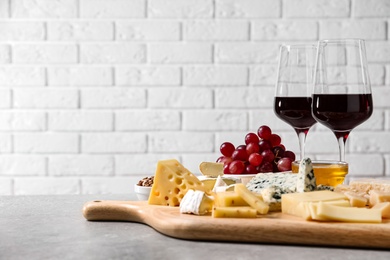 Cheese plate with honey, grapes and nuts on grey table against brick wall. Space for text