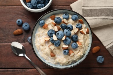 Tasty oatmeal porridge with blueberries and almond nuts served on wooden table, flat lay