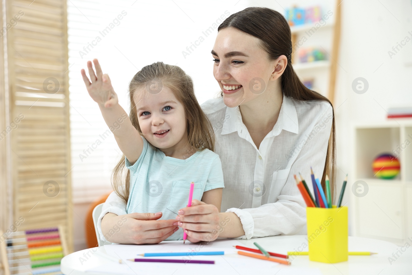 Photo of Mother and her little daughter drawing with colorful pencils at home