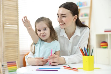 Mother and her little daughter drawing with colorful pencils at home