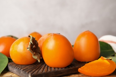 Photo of Delicious fresh persimmons and green leaves on wooden table, closeup