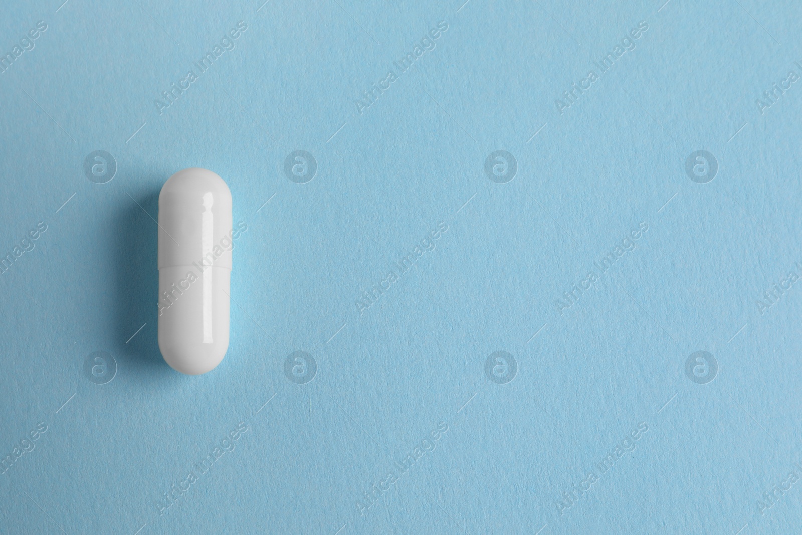 Photo of One white pill on light blue background, top view. Space for text