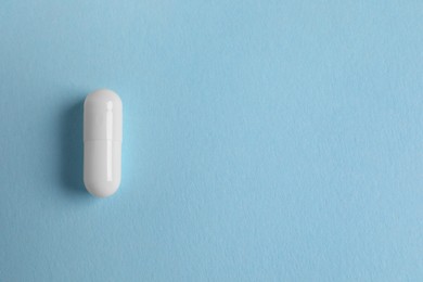 Photo of One white pill on light blue background, top view. Space for text