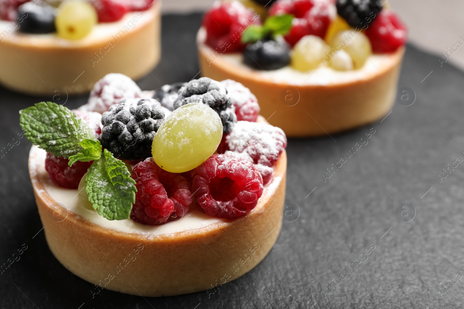 Photo of Delicious tartlets with berries on slate board, closeup