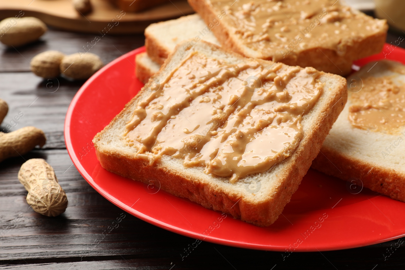 Photo of Delicious toasts with peanut butter on dark wooden table, closeup