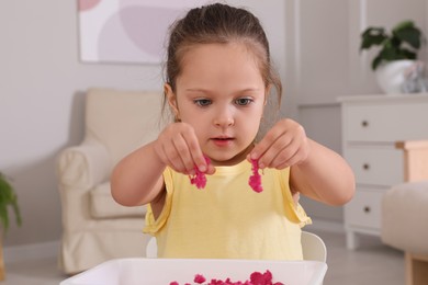 Cute little girl playing with bright kinetic sand at table in room