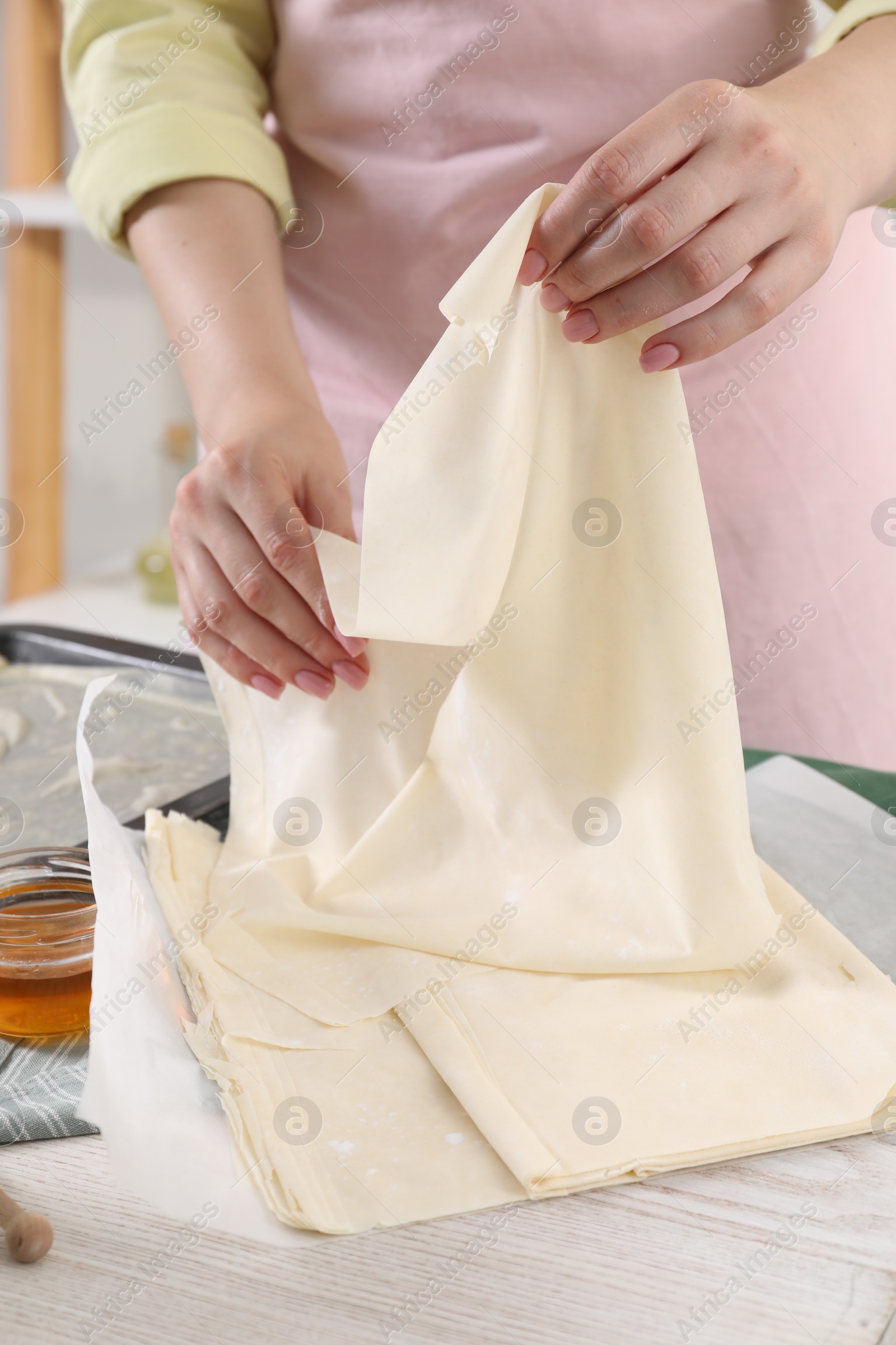 Photo of Making delicious baklava. Woman with dough at white wooden table, closeup