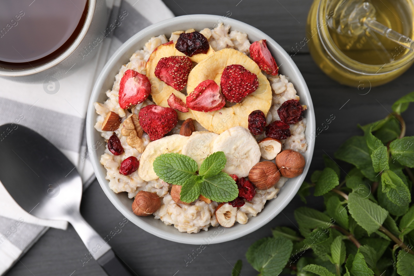 Photo of Oatmeal with freeze dried fruits, nuts and mint on grey wooden table, flat lay